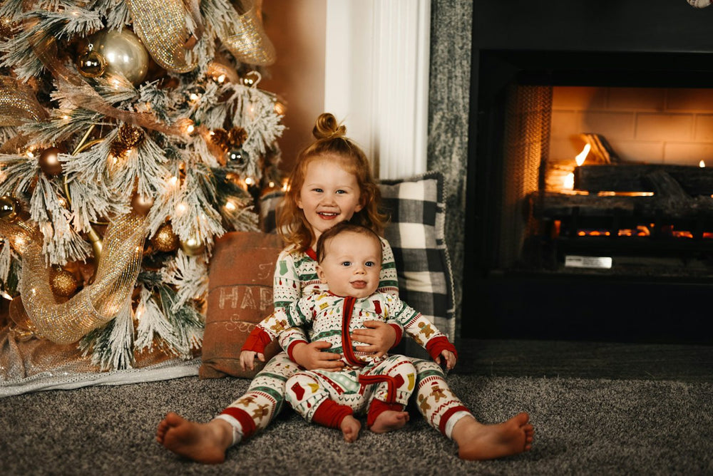 Two kids in matching Christmas pajamas by the tree